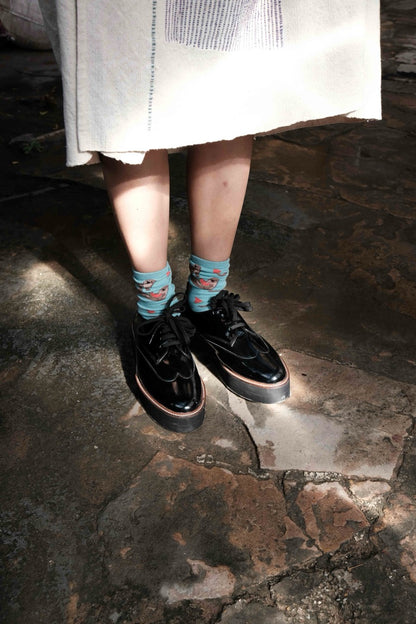 A pair of black Oxford shoes with a visible leather welt and upcycled tyre soles, worn by a person with socks peeking out from the top of the shoes.